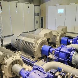 Maschinenraum mit großen Elektromotoren, blauen Pumpen und Schaltschränken.