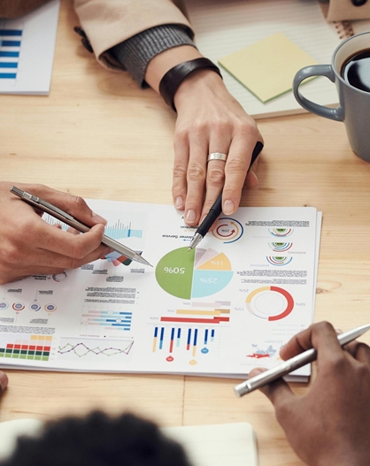 People jointly analyzing printed charts and business data at a meeting table.