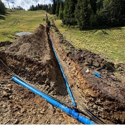 Construction trench with blue field pipelines in a meadow at the edge of a forest.